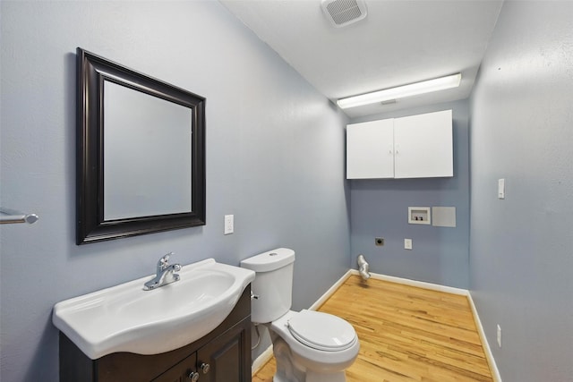 half bath featuring vanity, toilet, visible vents, baseboards, and wood finished floors