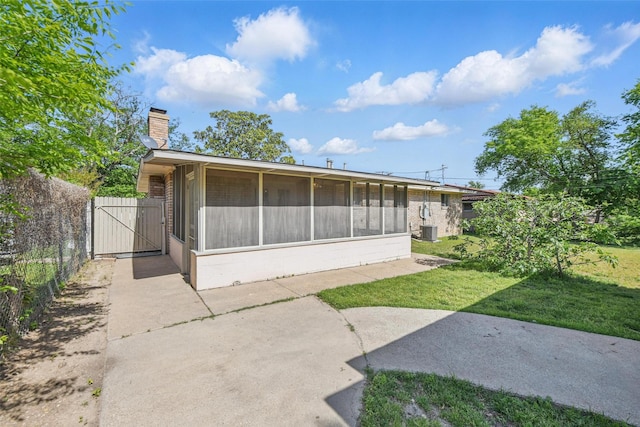 rear view of property featuring a chimney, a gate, a sunroom, central AC, and a lawn