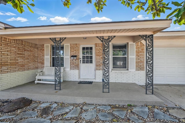 doorway to property featuring a porch, brick siding, and a garage