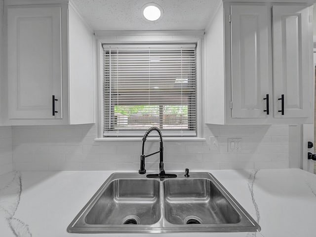 kitchen featuring backsplash, light countertops, a sink, and white cabinetry