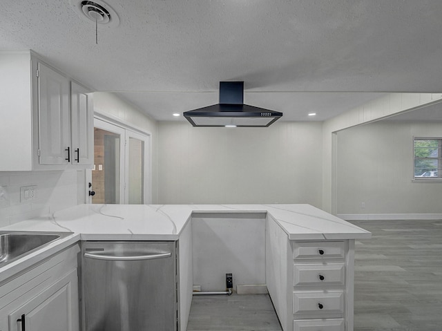 kitchen featuring light wood-type flooring, wall chimney range hood, a textured ceiling, white cabinetry, and stainless steel dishwasher
