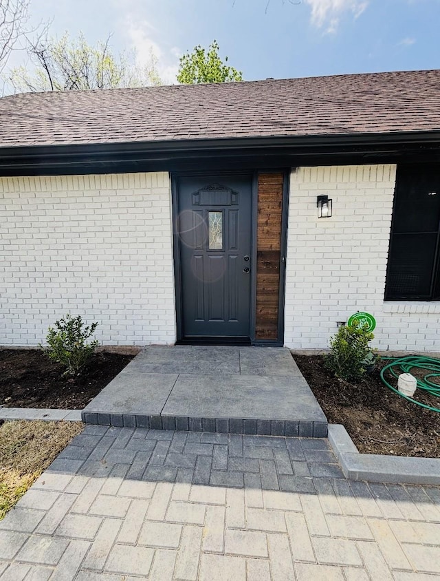 doorway to property featuring brick siding and a shingled roof