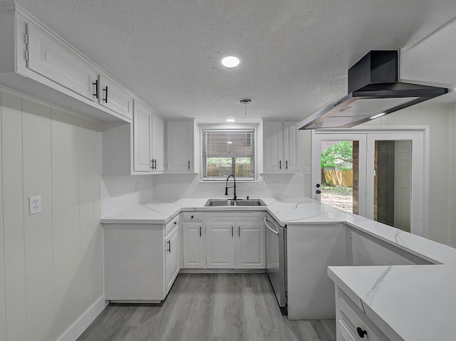 kitchen featuring light stone counters, light wood finished floors, a sink, and wall chimney range hood