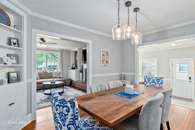 dining space featuring built in features, light wood-type flooring, crown molding, and a ceiling fan