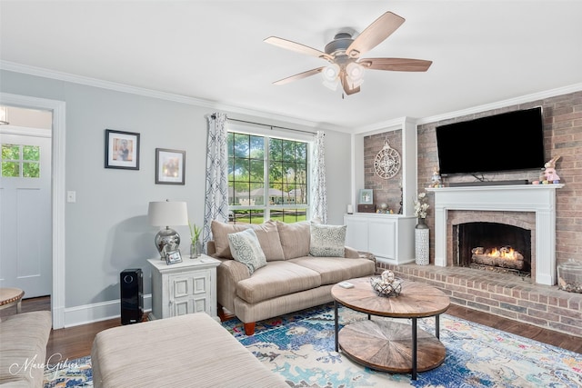 living room featuring baseboards, a brick fireplace, a ceiling fan, crown molding, and wood finished floors