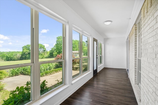 unfurnished sunroom with a healthy amount of sunlight, wood finished floors, and baseboards