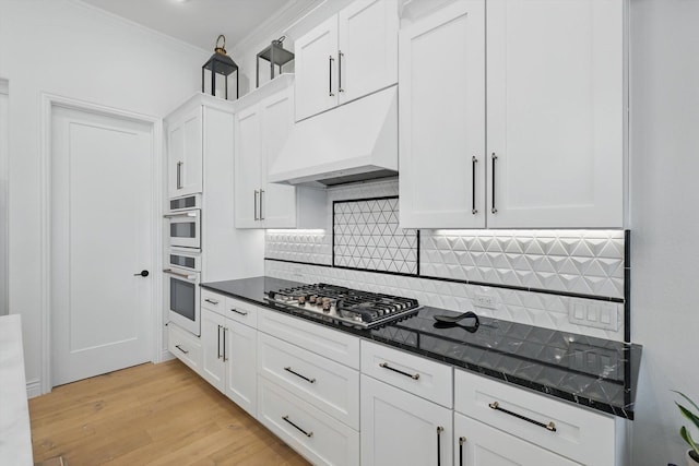 12424 Blue Granite Dr, Denton, TX 76207 - kitchen with under cabinet range hood, stainless steel gas cooktop, white cabinetry, light wood-type flooring, and decorative backsplash