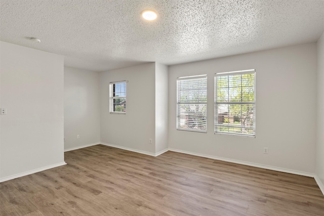 empty room featuring a textured ceiling, baseboards, and wood finished floors
