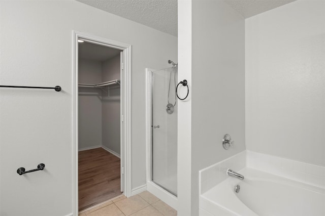 full bath featuring tile patterned floors, a spacious closet, a stall shower, and a garden tub