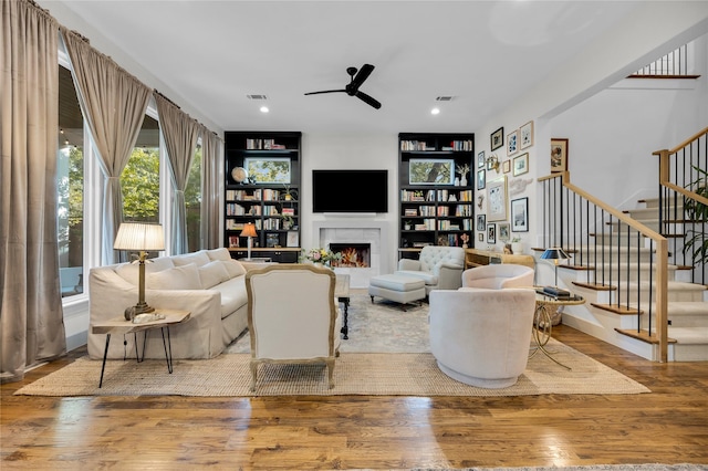 living room featuring wood finished floors, ceiling fan, visible vents, and stairs