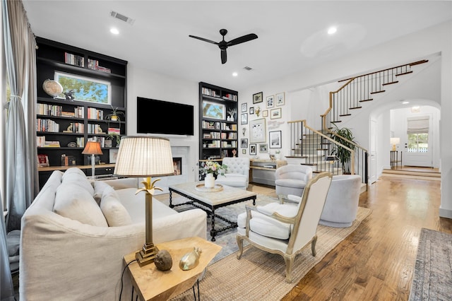 living room with stairway, visible vents, ceiling fan, arched walkways, and wood finished floors