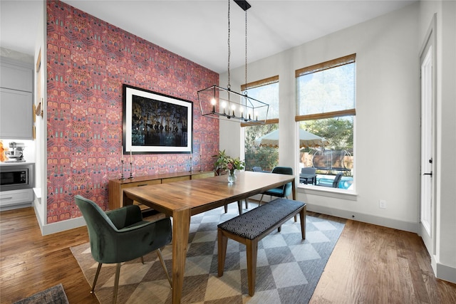 dining room featuring an inviting chandelier, baseboards, wallpapered walls, and wood finished floors