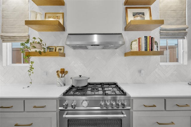 kitchen with high end range, backsplash, open shelves, and wall chimney exhaust hood