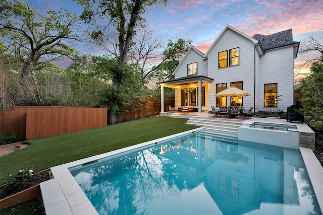 back of property at dusk featuring a yard, outdoor lounge area, fence, an in ground hot tub, and a fenced in pool