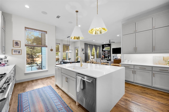 kitchen with light countertops, gray cabinetry, stainless steel appliances, a sink, and wood finished floors