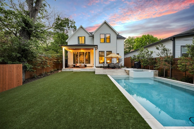 rear view of property featuring a fenced backyard, a pool with connected hot tub, a patio area, and a lawn