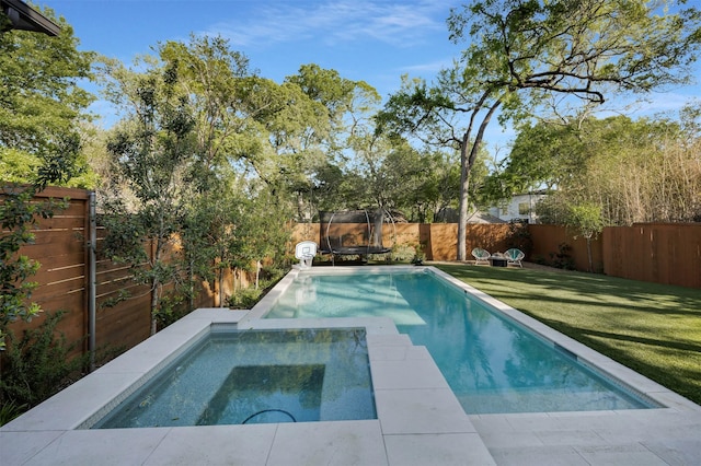 view of swimming pool with a trampoline, an in ground hot tub, a fenced backyard, and a lawn