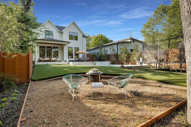 back of house with a patio area, an outdoor fire pit, a trampoline, a lawn, and fence