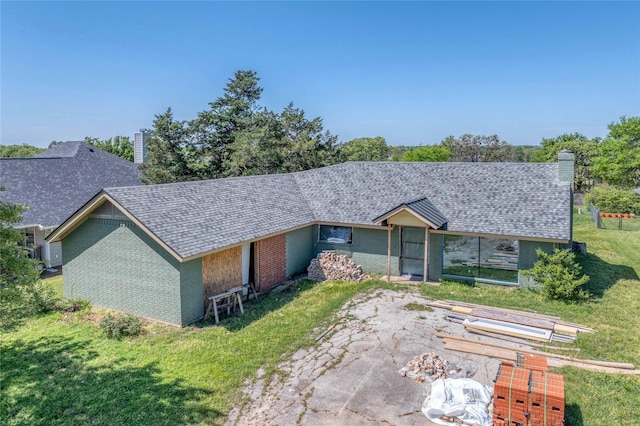 single story home featuring a chimney, a shingled roof, a front yard, and brick siding