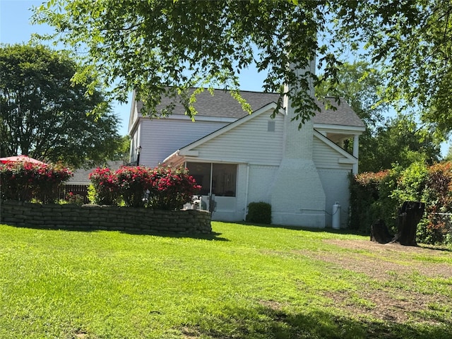 exterior space with brick siding, a sunroom, a lawn, and roof with shingles