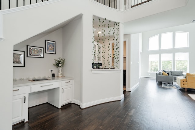 hallway with dark wood-style flooring, baseboards, and a high ceiling