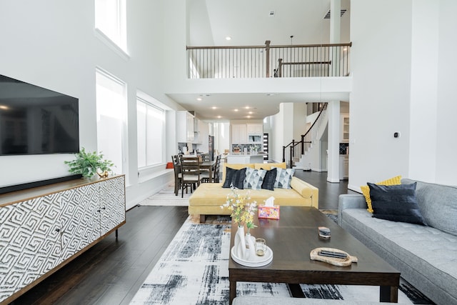 living area with a towering ceiling, dark wood-style floors, visible vents, and stairs