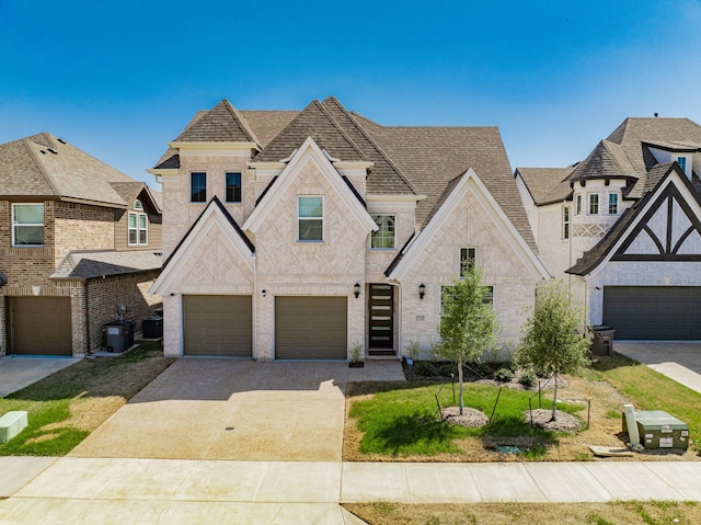 french country inspired facade featuring an attached garage, roof with shingles, driveway, and brick siding
