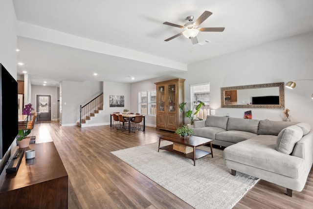 living area with visible vents, baseboards, wood finished floors, ceiling fan, and stairway