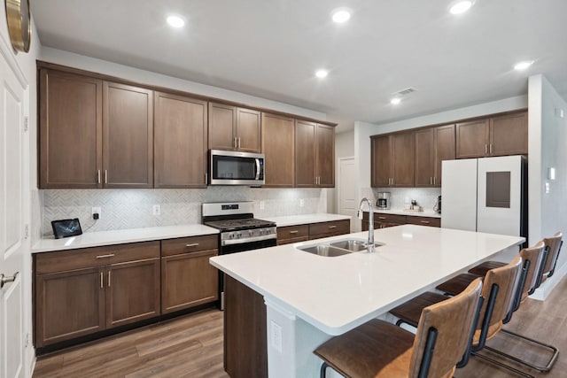 kitchen featuring a kitchen breakfast bar, wood finished floors, a sink, a kitchen island with sink, and appliances with stainless steel finishes