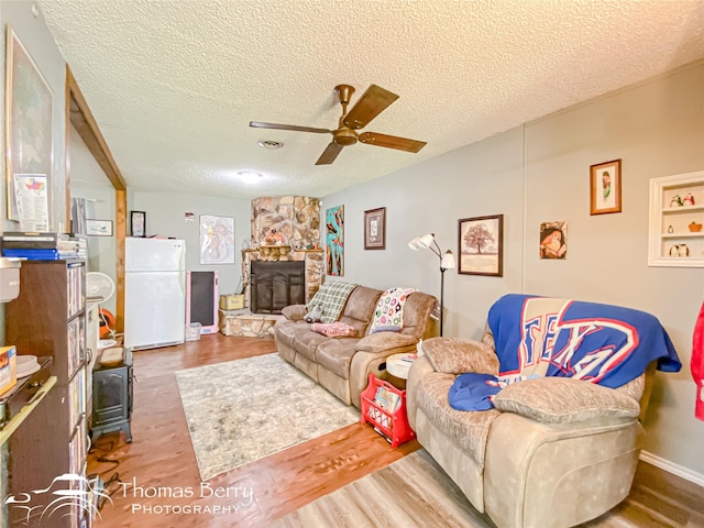 living room featuring a wood stove, a ceiling fan, wood finished floors, and a textured ceiling