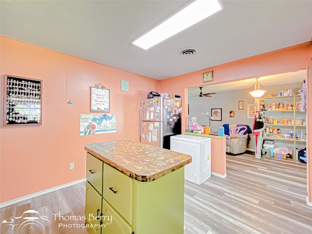 kitchen featuring freestanding refrigerator, green cabinetry, ceiling fan, light wood finished floors, and a center island