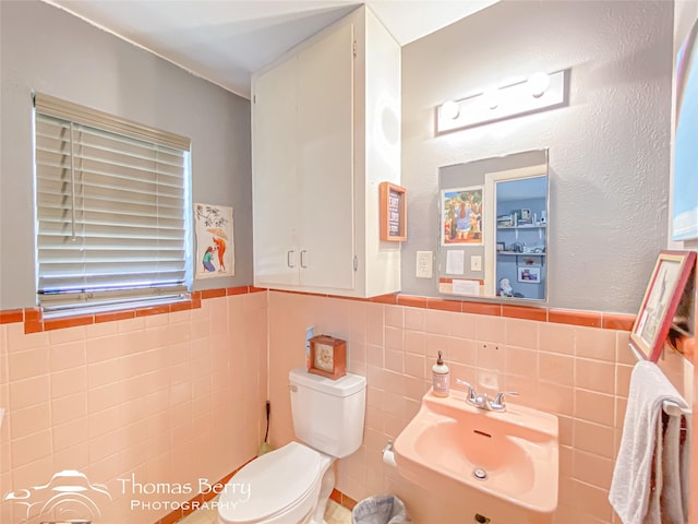 half bathroom with toilet, a wainscoted wall, and tile walls