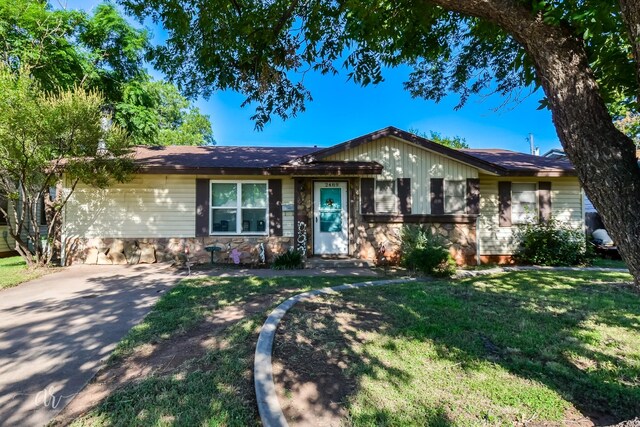 ranch-style house featuring a front yard, driveway, and stone siding