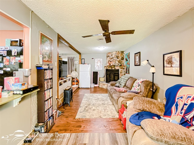 living area with wood finished floors, a ceiling fan, a stone fireplace, and a textured ceiling