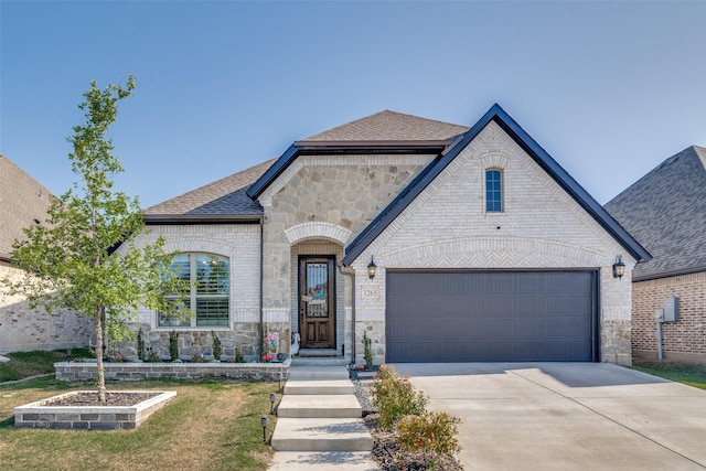 french country home with a shingled roof, stone siding, a garage, brick siding, and driveway
