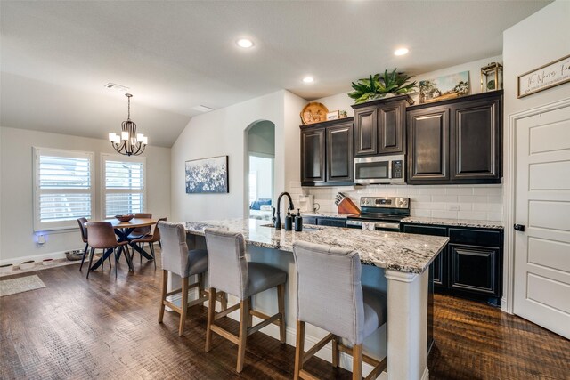 kitchen with arched walkways, a sink, appliances with stainless steel finishes, a kitchen bar, and backsplash