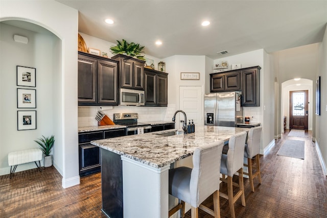 kitchen featuring tasteful backsplash, arched walkways, a sink, appliances with stainless steel finishes, and a kitchen bar