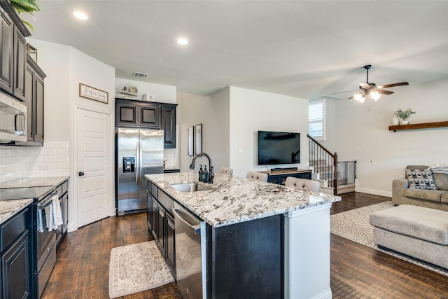 kitchen featuring a ceiling fan, a sink, stainless steel appliances, open floor plan, and dark wood-style floors