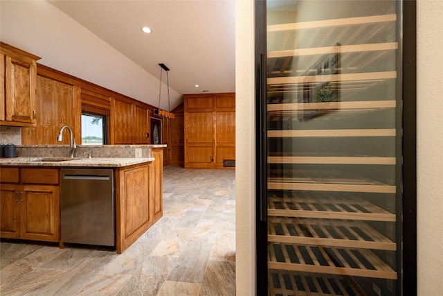 kitchen with a sink, brown cabinetry, light stone counters, dishwasher, and lofted ceiling
