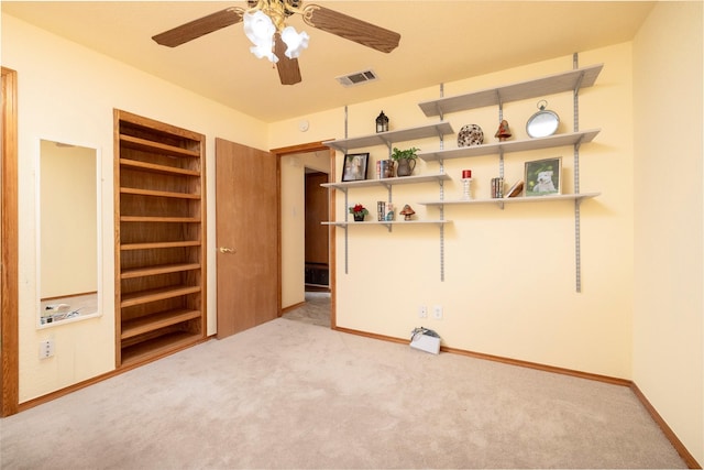 carpeted empty room with baseboards, visible vents, built in shelves, and ceiling fan