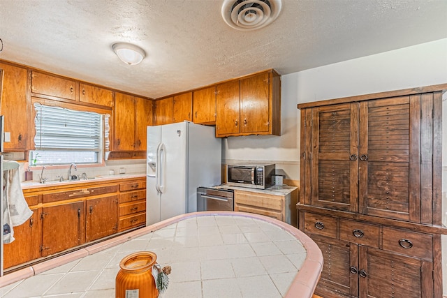1206 John Reagan St, Benbrook, TX 76126 - kitchen featuring white fridge with ice dispenser, brown cabinets, stainless steel microwave, a textured ceiling, and a sink