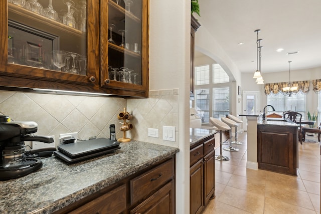 703 Sierra Ave, Mansfield, TX 76063 - kitchen with arched walkways, tasteful backsplash, dark stone counters, glass insert cabinets, and light tile patterned flooring