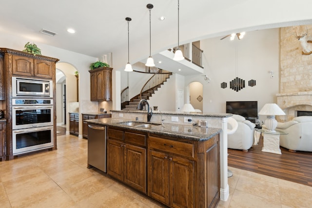 kitchen featuring arched walkways, a sink, open floor plan, appliances with stainless steel finishes, and dark stone counters