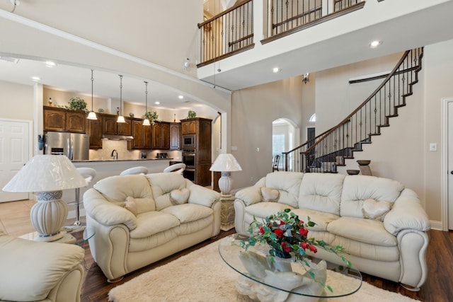 living area with arched walkways, a high ceiling, and wood finished floors