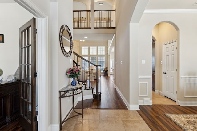 tiled foyer featuring arched walkways, baseboards, ornamental molding, and stairway