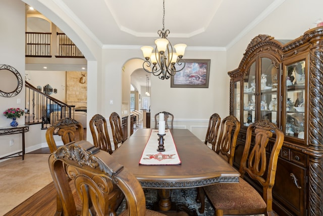 dining room with a raised ceiling, arched walkways, a chandelier, crown molding, and stairs