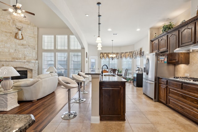 kitchen featuring ceiling fan with notable chandelier, tasteful backsplash, appliances with stainless steel finishes, under cabinet range hood, and open floor plan