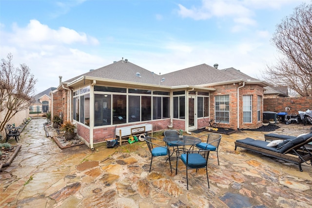 back of house featuring a sunroom, a patio area, fence, brick siding, and a shingled roof