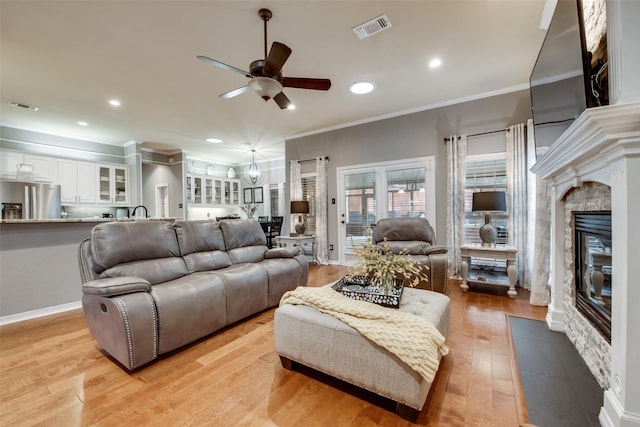 living area featuring crown molding, visible vents, a ceiling fan, and a fireplace with flush hearth