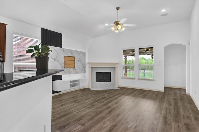 unfurnished living room featuring arched walkways, ceiling fan, wood finished floors, and a high end fireplace